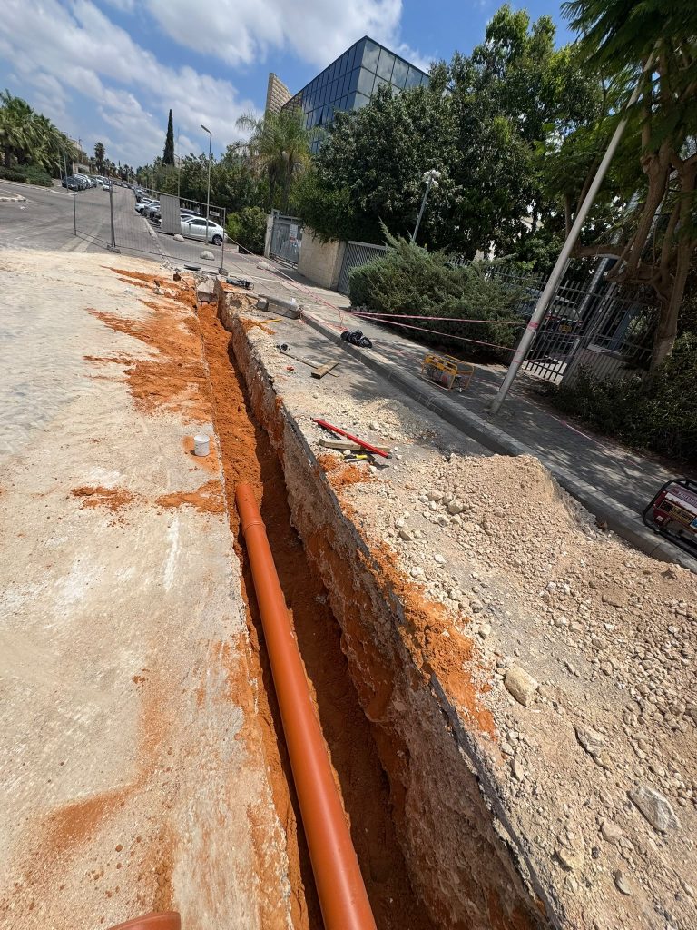 צינור ביוב כתום (PVC) מונח בתעלה פתוחה.