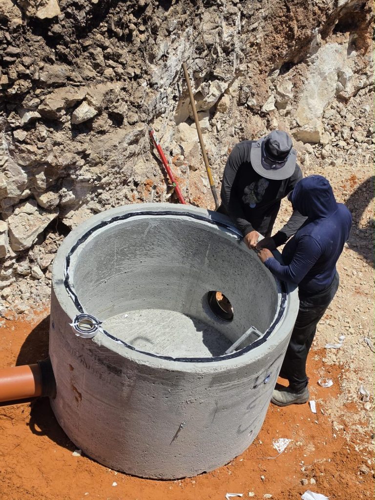 שני עובדים המבצעים את התקנת ואיטום טבעת הבטון, כאשר צינור ביוב כתום כבר מחובר לשוחה